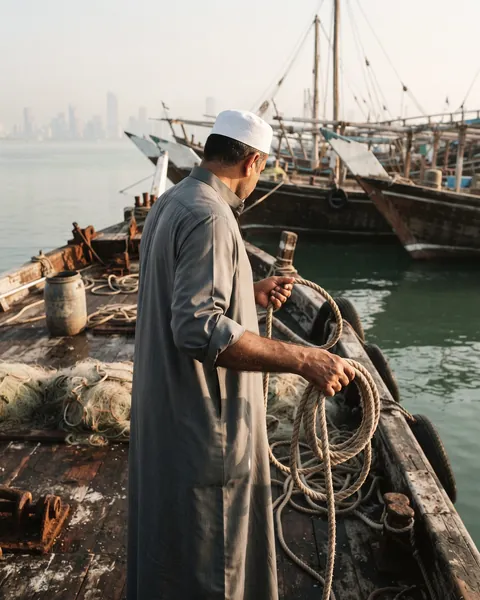 A man coiling rope on a wooden dhow in the harbor