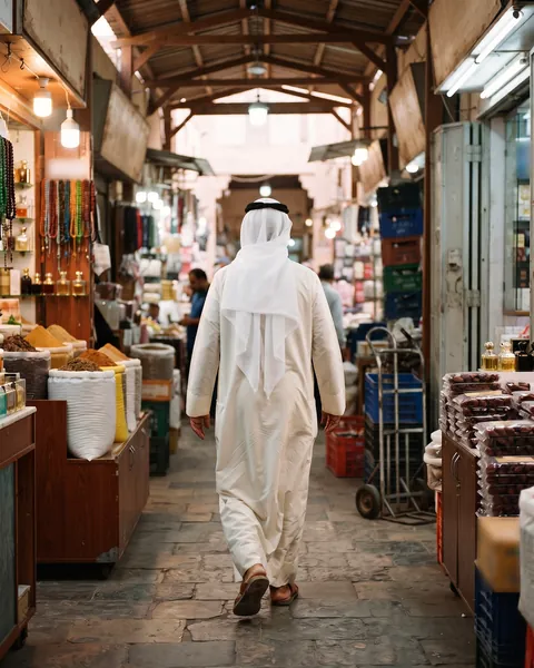A man in a dishdasha walking through Souq Al-Mubarakiya